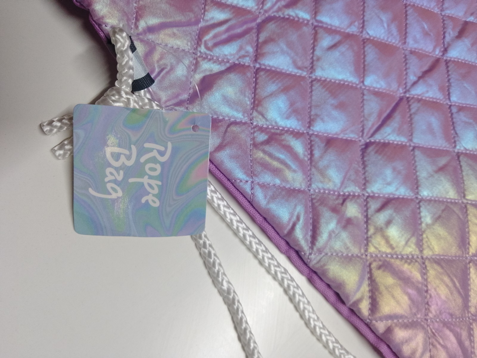 a purple quilted drawstring bag with an iridescent design and white drawstring