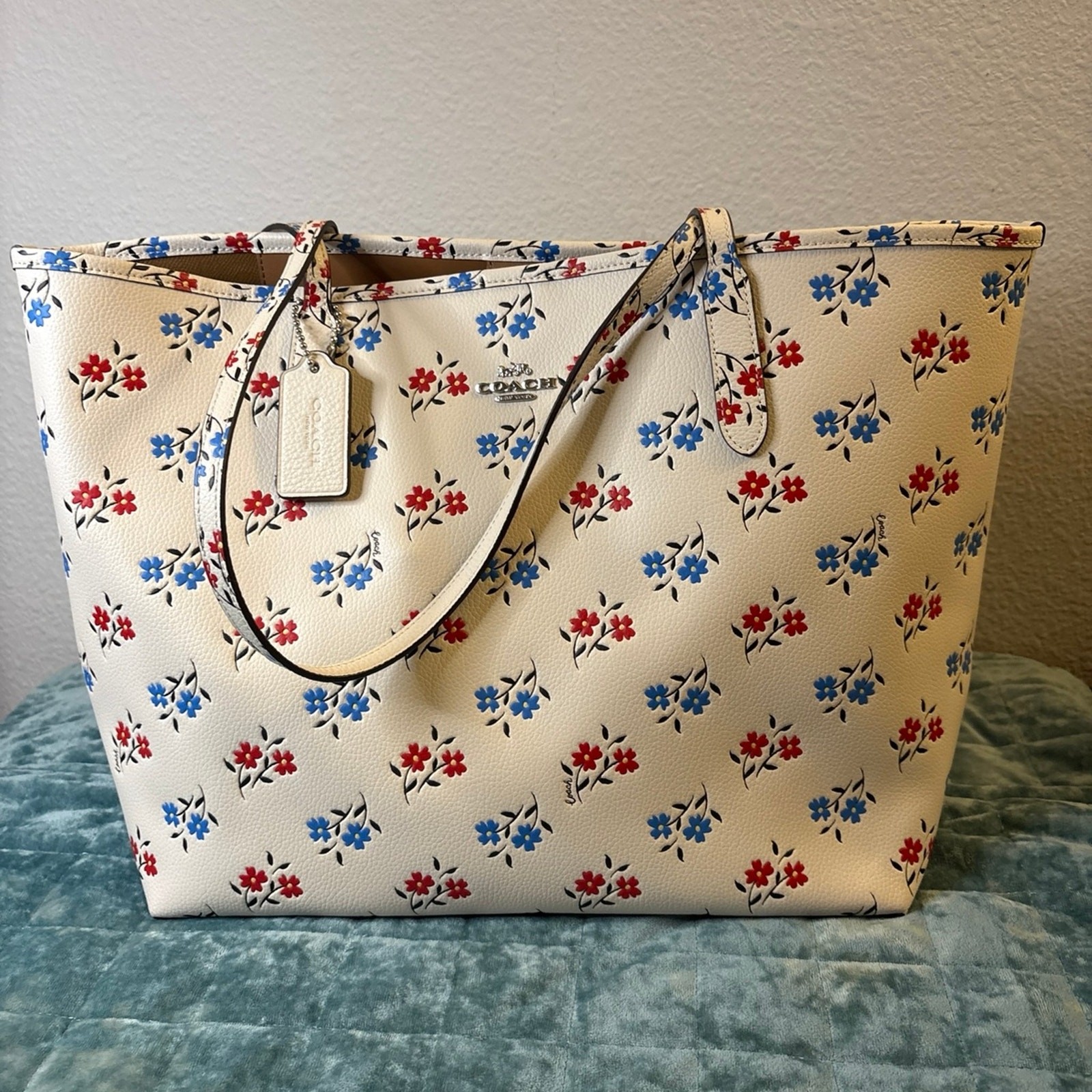 Coach floral tote bag with red, blue, and black flowers on a cream background